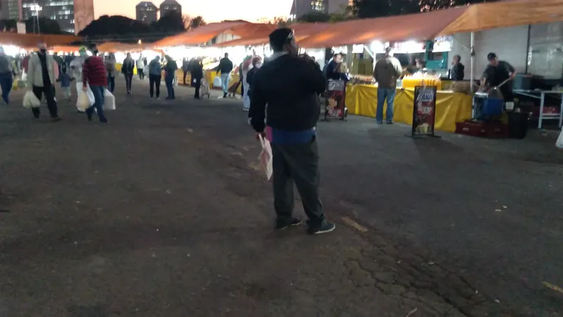 Pessoas circulam entre barracas iluminadas de uma feira no Largo da Epatur, em Porto Alegre, ao entardecer.