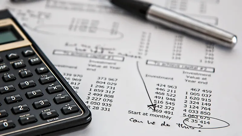 Calculadora e caneta sobre uma projeção impressa de investimentos com números e anotações à mão.