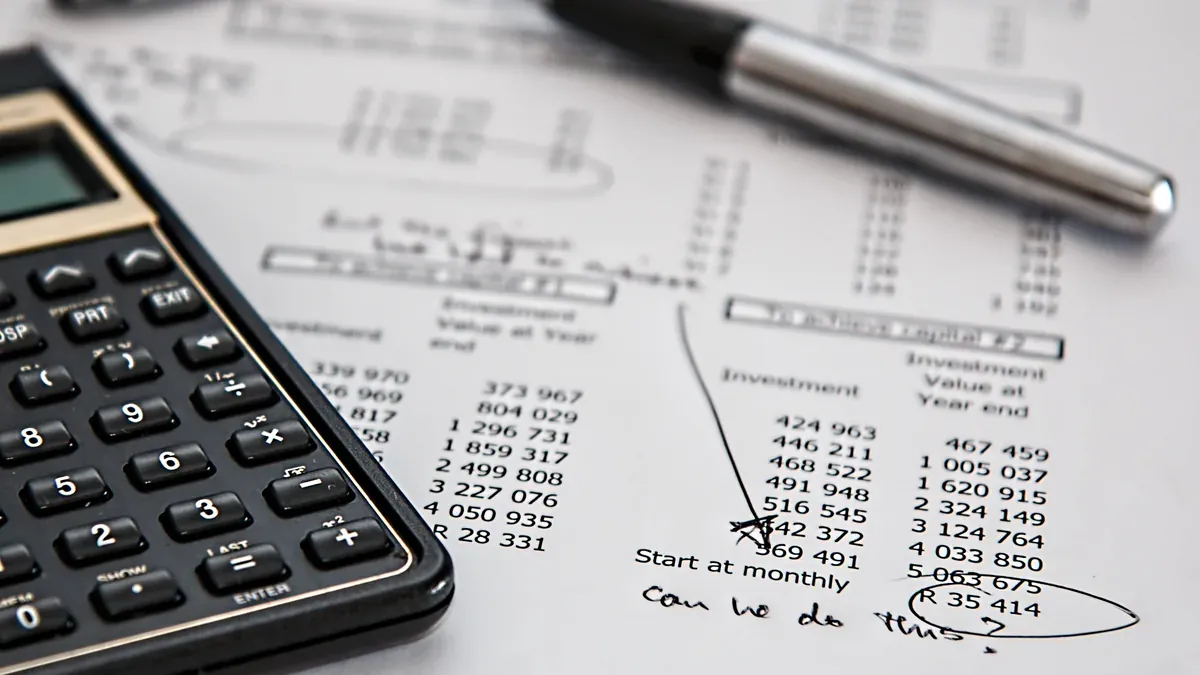 Calculadora e caneta sobre uma projeção impressa de investimentos com números e anotações à mão.