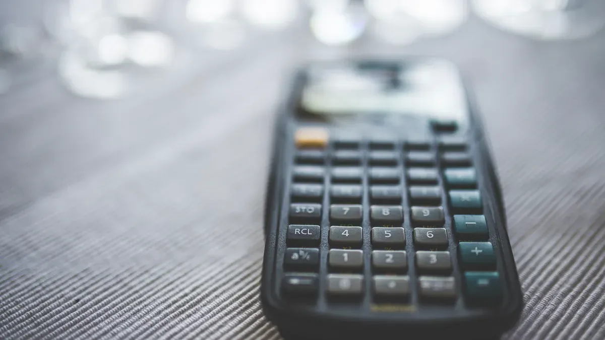 A dark calculator photographed close up on a textured desk, with a softly blurred background.