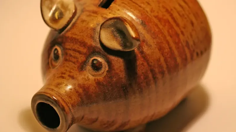 A brown glazed ceramic piggy bank seen close up on a warm cream background.