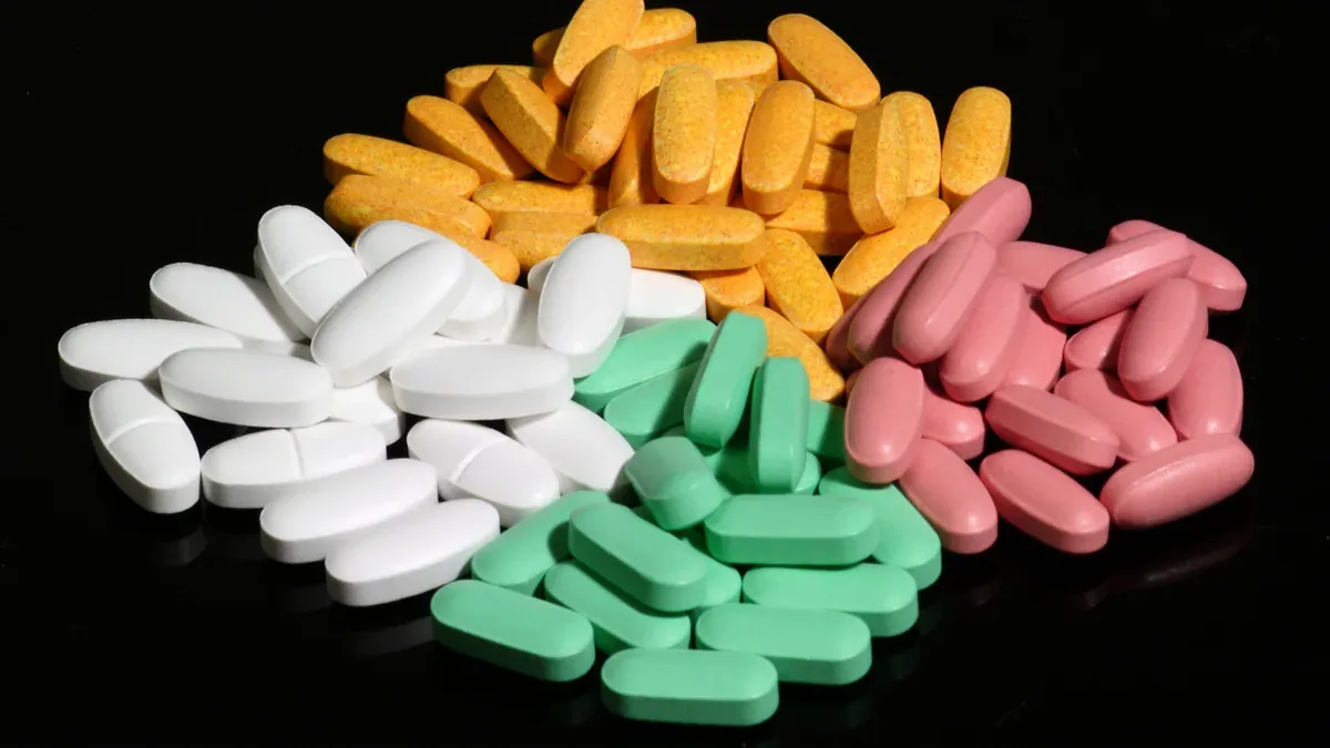Groups of yellow, pink, green and white tablets arranged on a black surface.