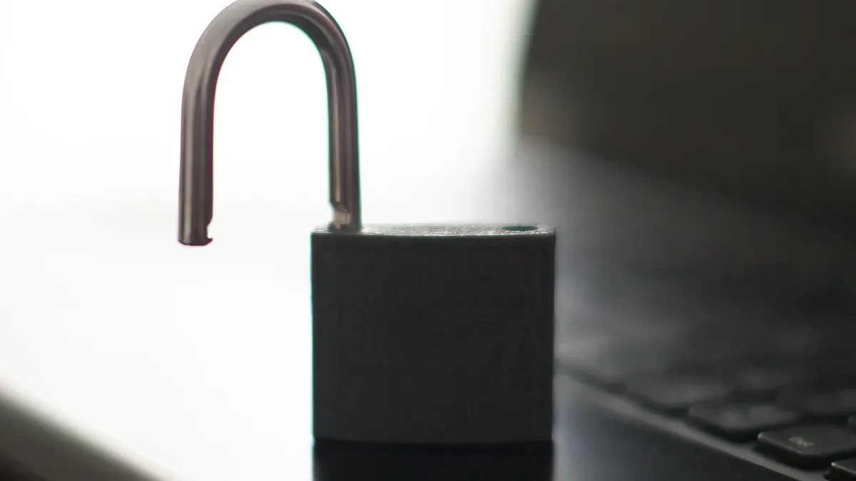 An open black padlock beside a laptop keyboard, photographed with a shallow depth of field.