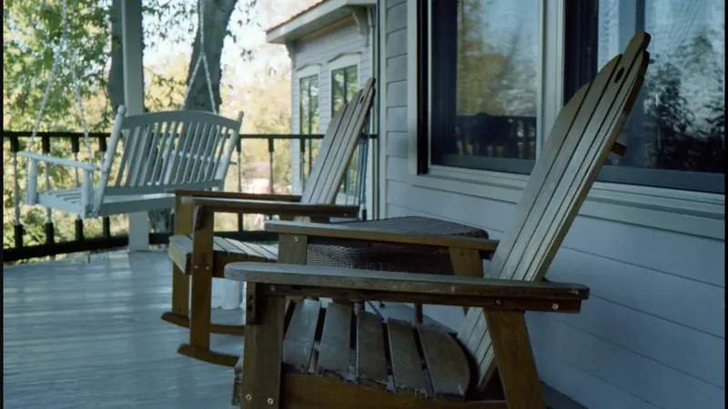 Wooden rocking chairs and a porch swing outside a white-sided home.
