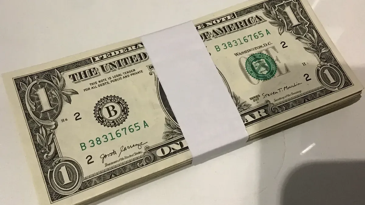 A neat bundle of U.S. one-dollar notes held together with a plain paper band on a light tabletop.